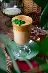 A glass of coffee with milk decorated with mint leaves on the table in a cafe, dalgona coffee, vertical photo