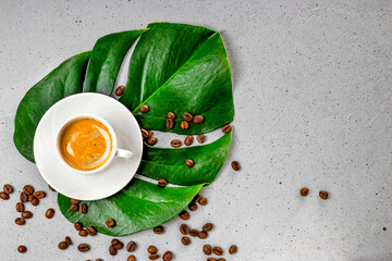 Cup of black coffee and coffee beans on monstera leaf and gray concrete background top view