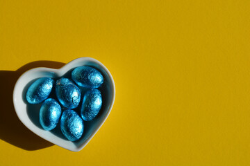 Heart and blue foil wrapped Easter eggs isolated on yellow background