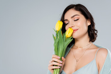Young woman smelling yellow tulips isolated on grey