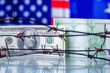 US Dollar and EU currency wrapped in barbed wire against United States and European Union flags as symbol of joint economic warfare, sanctions and embargo busting. Selective focus on Dollar banknote