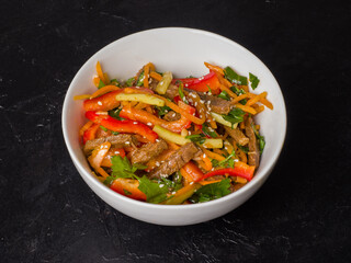 Korean salad with beef and peppers. White bowl on black background