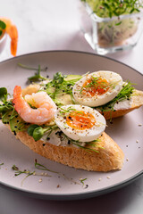 Breakfast with bruschetta with shrimps, eggs and microgreens in a plate