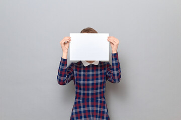 Woman is holding white blank paper sheet in front of her face