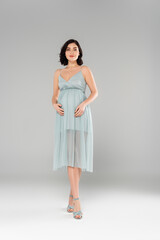 Pretty pregnant woman in dress looking at camera on grey background