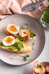 Breakfast with bruschetta with shrimps, eggs and microgreens in a plate