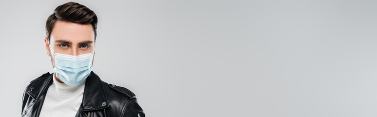 Young man in leather jacket and medical mask looking at camera isolated on grey, banner