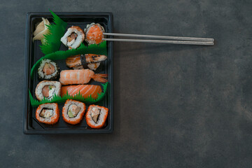 Set of sushi and rolls at delivery box with сhopsticks on dark background 