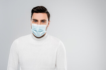 Young man in medical mask looking at camera isolated on grey