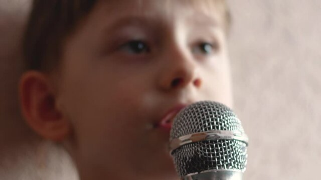 Close-up preschooler caucasian portrait with microphone sings a song. The child sings karaoke. Happy kid sings a song. Young vocalist. Selective focus, shallow depth of field