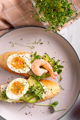 Breakfast with bruschetta with shrimps, eggs and microgreens in a plate