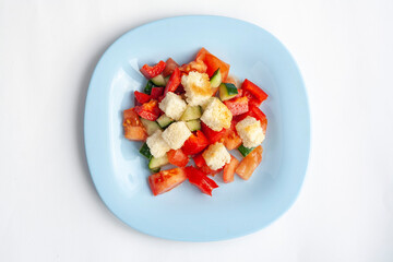 Vegetable salad with crackers in a blue plate, isolated on a white background, top view