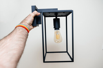 POV Male hand looking at vintage filament light bulb on box lantern wall light vintage style with...
