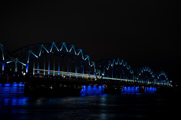 Fototapeta na wymiar Illuminated railway bridge over Daugava river in Riga, Latvia. Night cityscape.