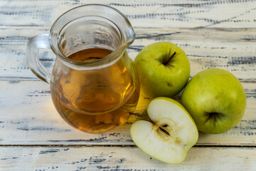 Green apples and jug with apple juice on wooden background