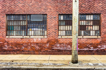 Fototapeta na wymiar Thick wooden telephone pole in front of vintage red brick warehouse industrial building with rectangle windows in urban Chicago