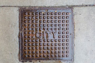 Vintage manhole cover on sidewalk on wet day in urban Chicago