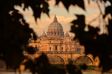 St. Peter's Basilica seen through the foliage of a tree near the river bank of the Tiber (Tevere),...