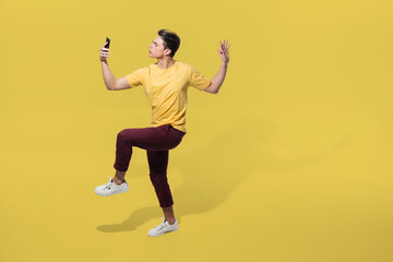 Fototapeta na wymiar Taking selfie. High angle view of young man on yellow background. Boy in motion. Human emotions and facial expressions concept. Full length portait, copyspace for ad. Fashion, retro style.