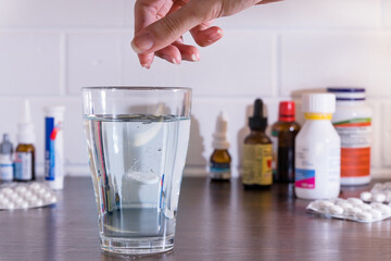 Throw pills in a glass against the background of pills and medications. Water poured into a glass with medicine. Throw the pills in the water.
