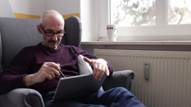 Mann sitzt auf Sessel und schaut Sport auf dem Tablet