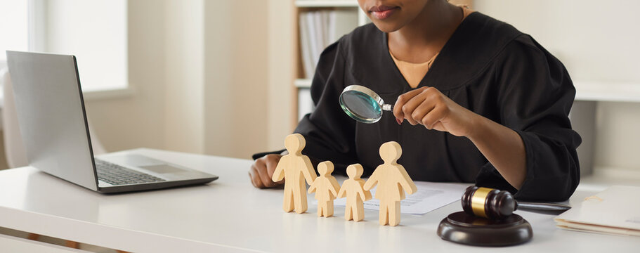 African American Judge Looking Through Magnifying Glass At Wood Family Figure