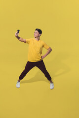 Fototapeta na wymiar Taking selfie on the go. High angle view of young man on yellow background. Boy in motion. Human emotions and facial expressions concept. Full length portait, copyspace for ad. Fashion, retro style.