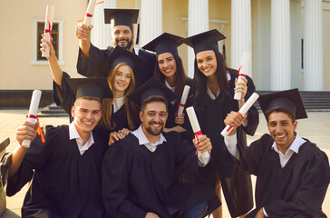 Collective photo of smiling boys and girls students university graduates celebrating getting diplomas with university building at background. Successful univesity graduation concept