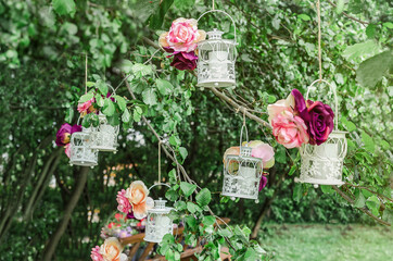 Beautiful lanterns with candles, decorated with roses and ribbons hang on a tree in a garden