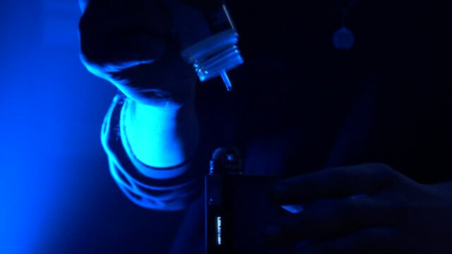 The process of filling the vape with liquid, on the bar counter is illuminated with blue light by hand