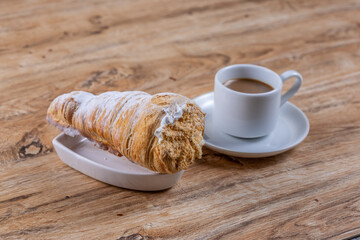  A cup of coffee next to delicious aromatic puff pastry cone with protein cream