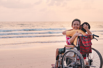 Mother and special child on wheelchair on the sea beach with sunset on travel time in holiday...