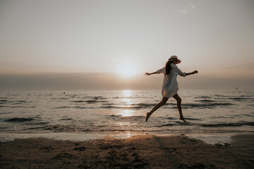 Fototapeta premium A girl runs along the waves at sunset. Silhouette of a slender woman at sunset by the sea.