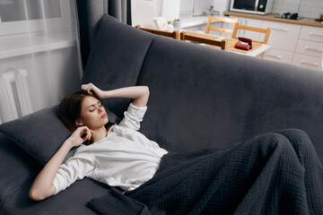 Fototapeta premium a woman in a white t-shirt lies on the sofa under a blanket and gestures with her hands