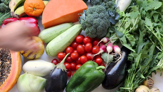 Male hand takes red tomato and broccoli on healthy food clean eating selection: fruit, vegetable, pumpkin, papaya superfood, leaf vegetable
