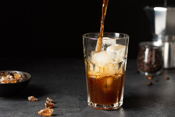 Pouring coffee into a glass with ice cubes.