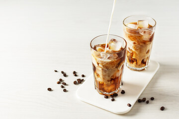 Pouring milk into glass with iced coffee.
