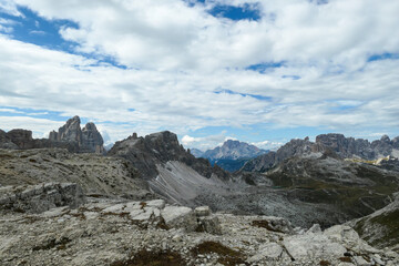 A panoramic view on a valley in Italian Dolomites. There is a massive mountain in front, with very steep and sharp slopes. In the back there are smaller mountain chains. Raw and desolated landscape