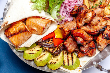 Mixed grill meat fried vegetables and grilled salmon fish fillets decoration in warm dish. Assorted delicious grilled kebab served with herbs on platter. Restaurant menu barbecue plate Bbq party meal