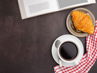 Obraz na płótnie Canvas Top view of a book with croissant on a plate and a white coffee cup placed on a dark gray background. Space for text. Concept of relaxation