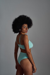 Confident young african american woman with afro hairstyle wearing blue underwear looking at camera while posing isolated over grey background