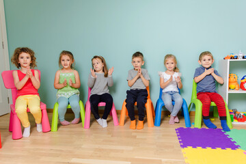 Kids are sitting on the colorful chairs, clapping hand