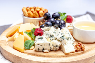 Board with different types of cheese. Cheeses mix set dor blu chedar parmesan brie honey sauce finger bread and grape on wooren palte. Restaurant menu breakfast plate. Healthy snack assortment.