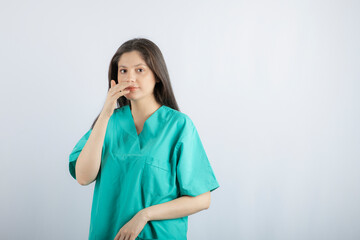 Young beautiful nurse holding her hand to her mouth and looking at camera