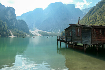 A small wooden house build on pillars above the Pragser Wildsee, a lake in South Tyrolean Dolomites. High mountain chains around the lake. Dense forest at the shore. Autumn vibe. Serenity and calmness