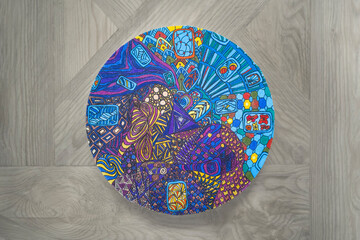 Step-by-step instructions for DIY round wall clock on canvas in technique of zentangle drawing pattern: step 5.1- colored painted,coated with varnish,drying,on gray wooden background.Copy space