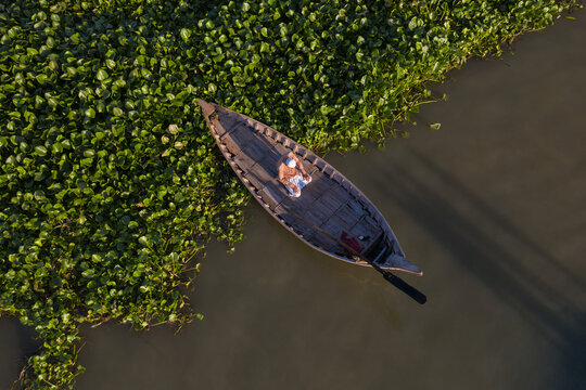 Aerial view of a man praying alone on a small traditional canoe along Buriganga river in Dhaka province, Bangladesh.