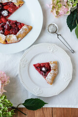 Delicious freshly baked vegan strawberry and cherry galette on wooden rustic background with hydrangea flowers, top view. Sweet food, summer dessert.