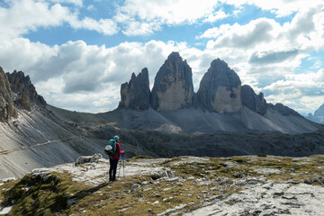 Fototapeta premium A woman in hiking outfit enjoying the view on the famous Tre Cime di Lavaredo (Drei Zinnen), mountains in Italian Dolomites. Desolated and raw landscape, full of lose stones. Overcast. Achievement