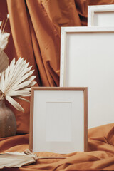 White blank wooden frames in an artistic interior with a mustard-colored cloth, near dried flowers in a clay vase